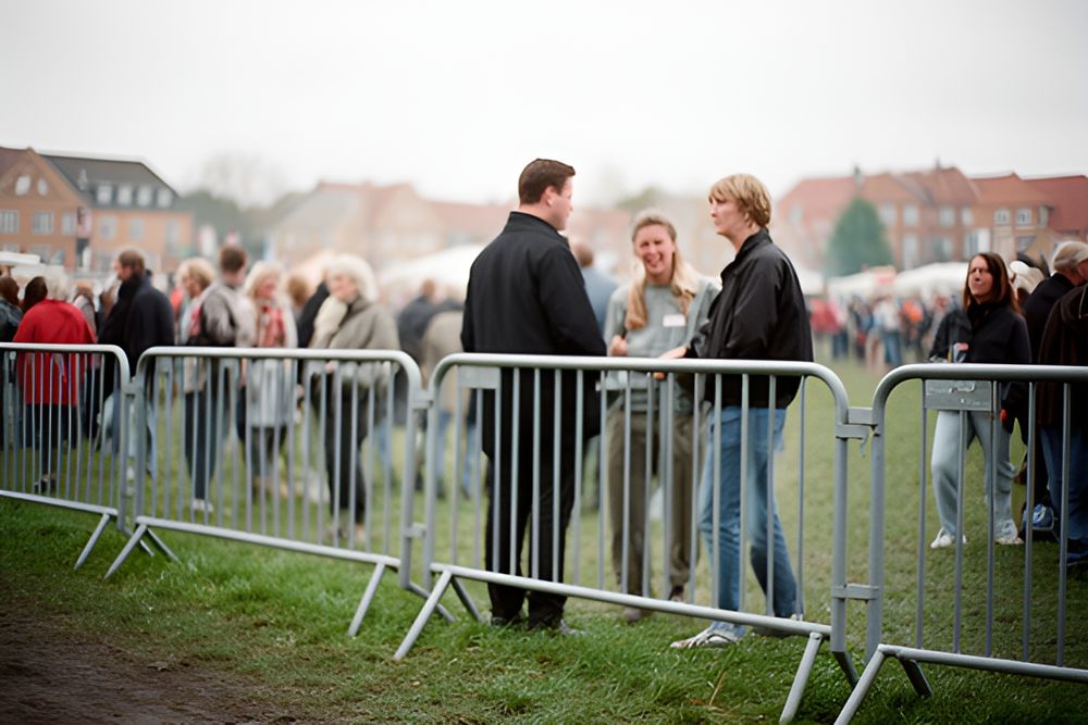 Gæster på en græsmark bag grå afspærringshegn ved en byfest